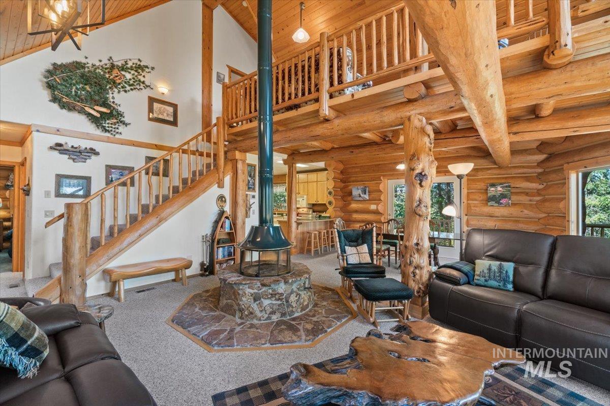 3725 Rim Road New Meadows, ID 83654 - Photo 6 of 50 Carpeted living area with high vaulted ceiling, a wooden ceiling with exposed beams, a wood stove, stairs, and rustic walls