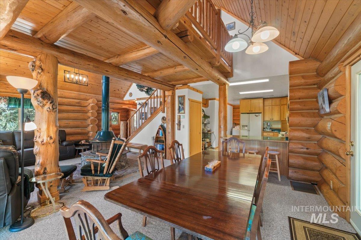 3725 Rim Road New Meadows, ID 83654 - Photo 8 of 50 Dining room with log walls, light colored carpet, a wooden ceiling with exposed beams, stairway, and a chandelier