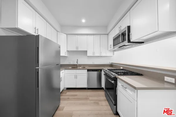 a kitchen with stainless steel appliances granite countertop white cabinets a sink a stove a refrigerator and white cabinets