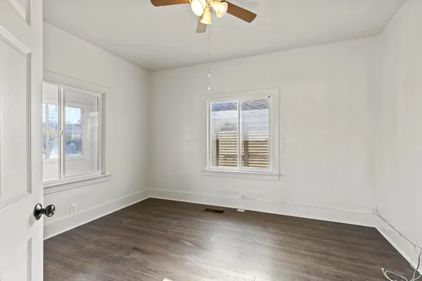 an empty room with wooden floor chandelier fan and windows
