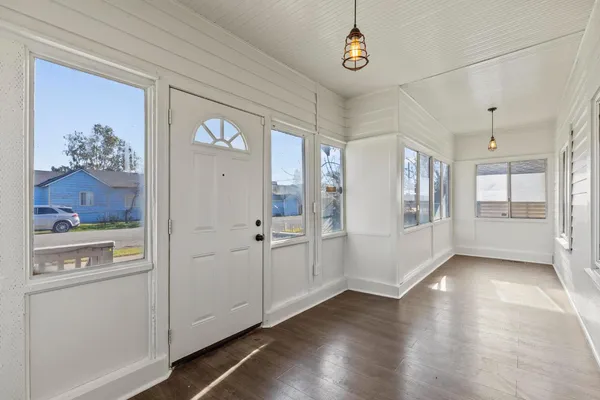 a view of a hallway to an empty room with wooden floor and a window