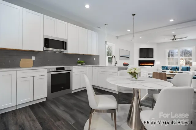 a kitchen with stainless steel appliances a stove a sink a microwave a refrigerator white cabinets and couches with wooden floor