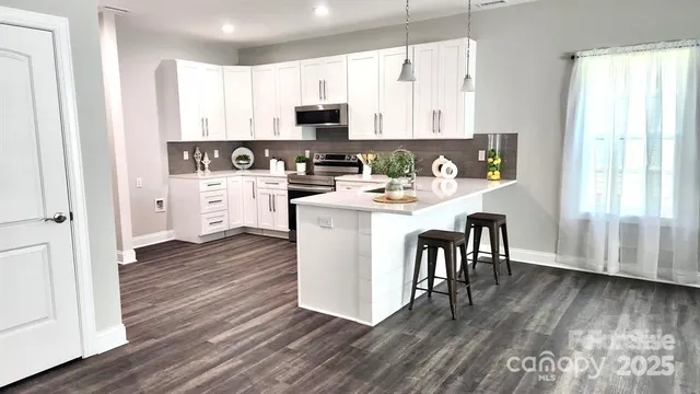 a kitchen with stainless steel appliances a white stove top oven a sink and white cabinets with wooden floor