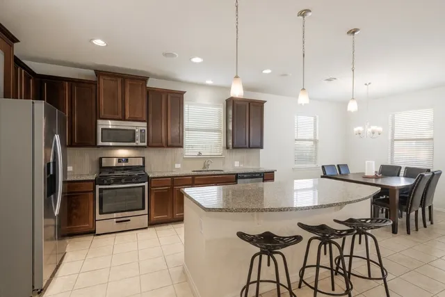 a kitchen with stainless steel appliances granite countertop a stove a sink a microwave a island with a dining table and chairs