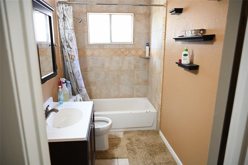 1352 Simpson Drive Hurst, TX 76053 - Photo 35 of 40 Full bathroom featuring a single vanity with a white countertop and dark wood-finish cabinetry, a toilet, and a bathtub with tile surround and an integrated shower