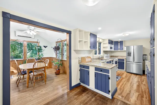 a open kitchen with stainless steel appliances granite countertop a stove top oven a refrigerator a dining table and chairs with wooden floor