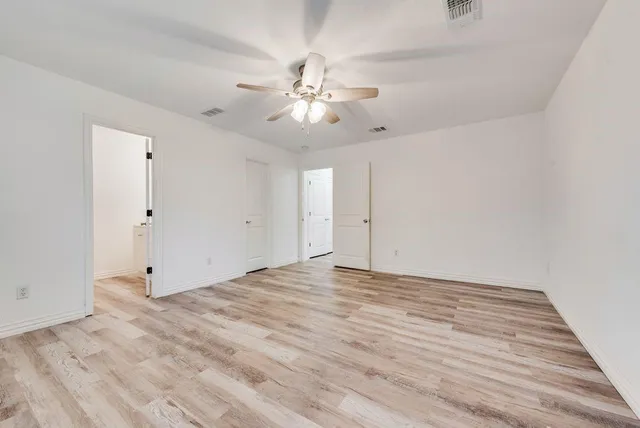 a view of an empty room with chandelier fan and wooden floor