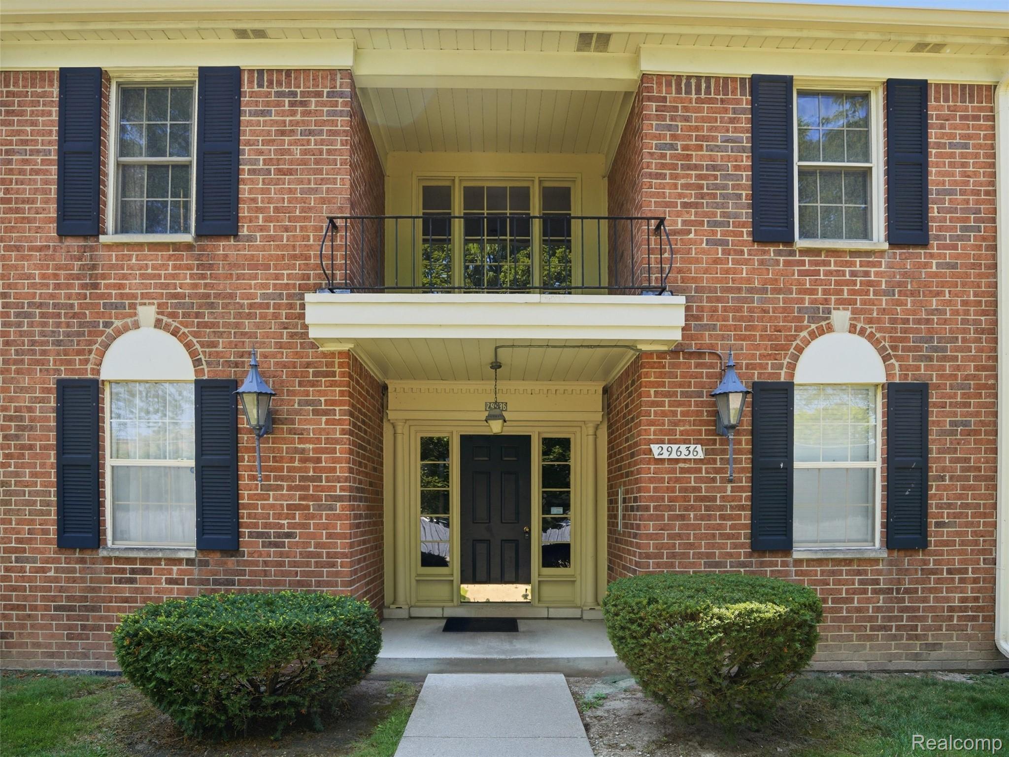 Brick exterior with dark shutters, an arched window detail, and an upper-level balcony with a black wrought iron railing