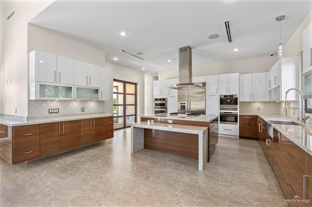 1425 Encanto Road, Unit SERVICE Weslaco, TX 78596 - Photo 12 of 45 Kitchen featuring backsplash, brown cabinetry, light stone counters, white cabinetry, and a large island