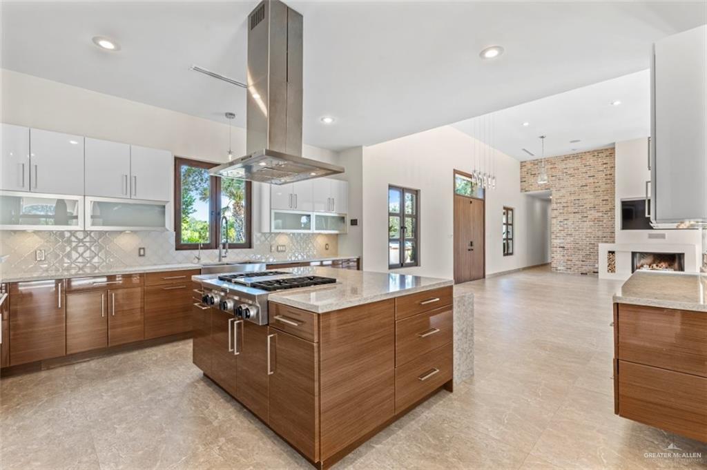 1425 Encanto Road, Unit SERVICE Weslaco, TX 78596 - Photo 13 of 45 Kitchen with brown cabinets, a kitchen island, tasteful backsplash, light stone countertops, and island range hood