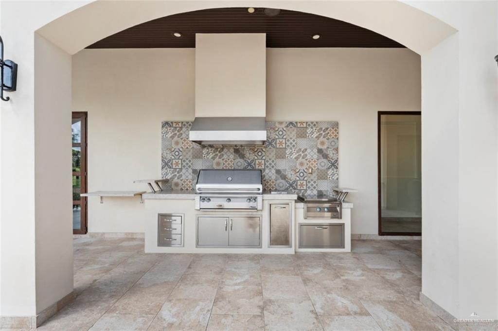 1425 Encanto Road, Unit SERVICE Weslaco, TX 78596 - Photo 8 of 45 Outdoor kitchen with arched walkways, tasteful backsplash, wall chimney exhaust hood, and light countertops