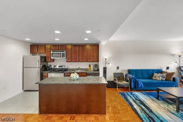 a living room with stainless steel appliances furniture a rug and a kitchen view