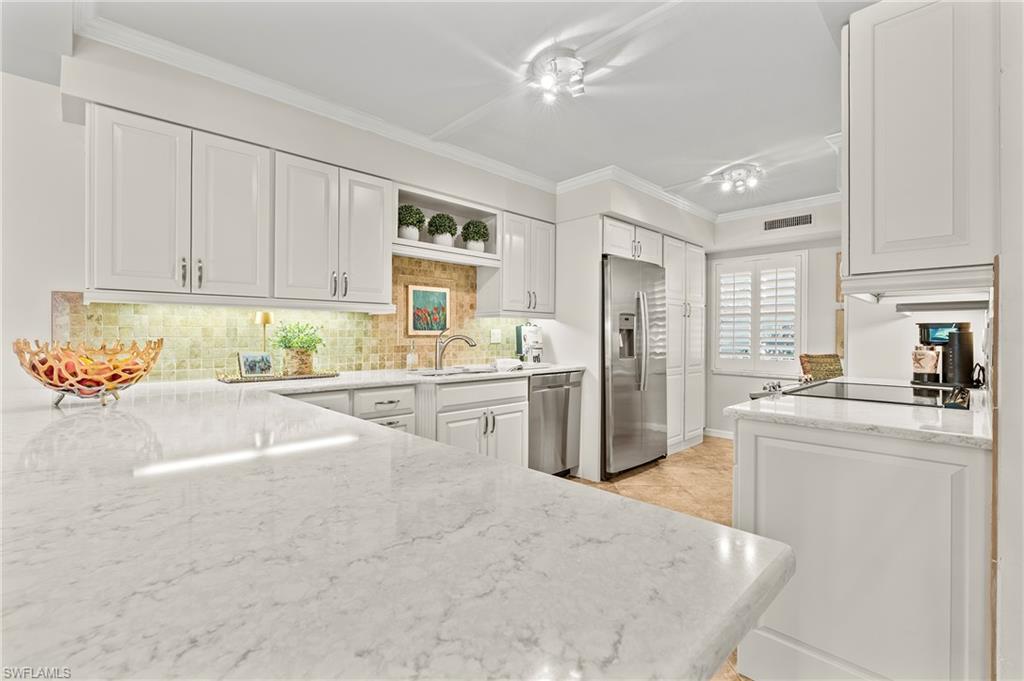 4155 Crayton Road, Unit 107 Naples, FL 34103 - Photo 35 of 36 Kitchen with tasteful backsplash, ornamental molding, stainless steel appliances, white cabinets, and kitchen peninsula