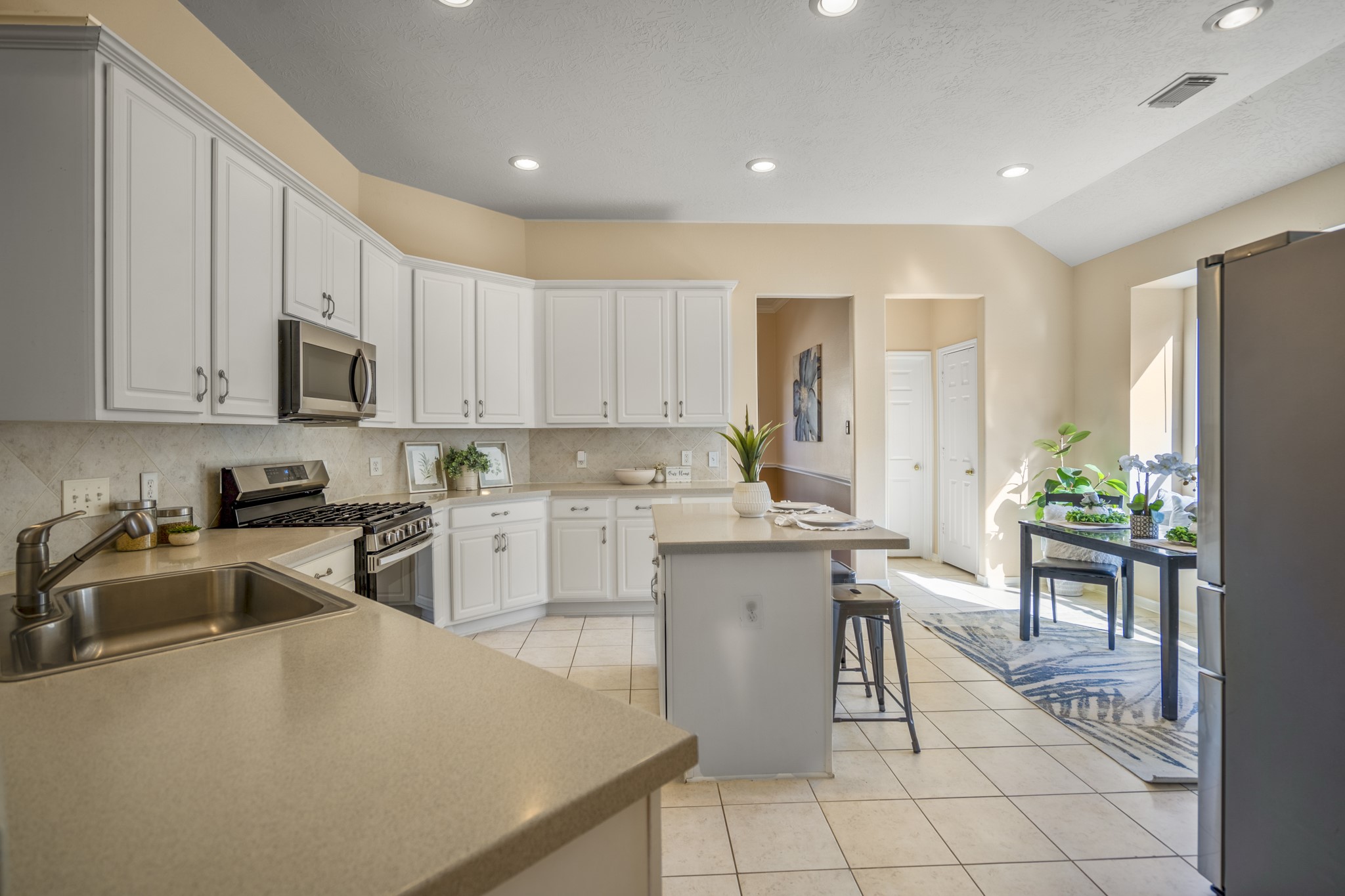 21107 Coldde Meadow Lane Spring, TX 77379 - Photo 11 of 50 Standing in the kitchen, this view shows the main workspace with generous counter space, abundant cabinetry, and an island that adds extra prep and serving room. Just beyond, the breakfast area offers a bright spot for casual meals beside the windows. The opening on the left connects back to the formal dining room, while the hallway to the right leads to the pantry and the laundry room, keeping everyday storage and chores conveniently close to the kitchen.