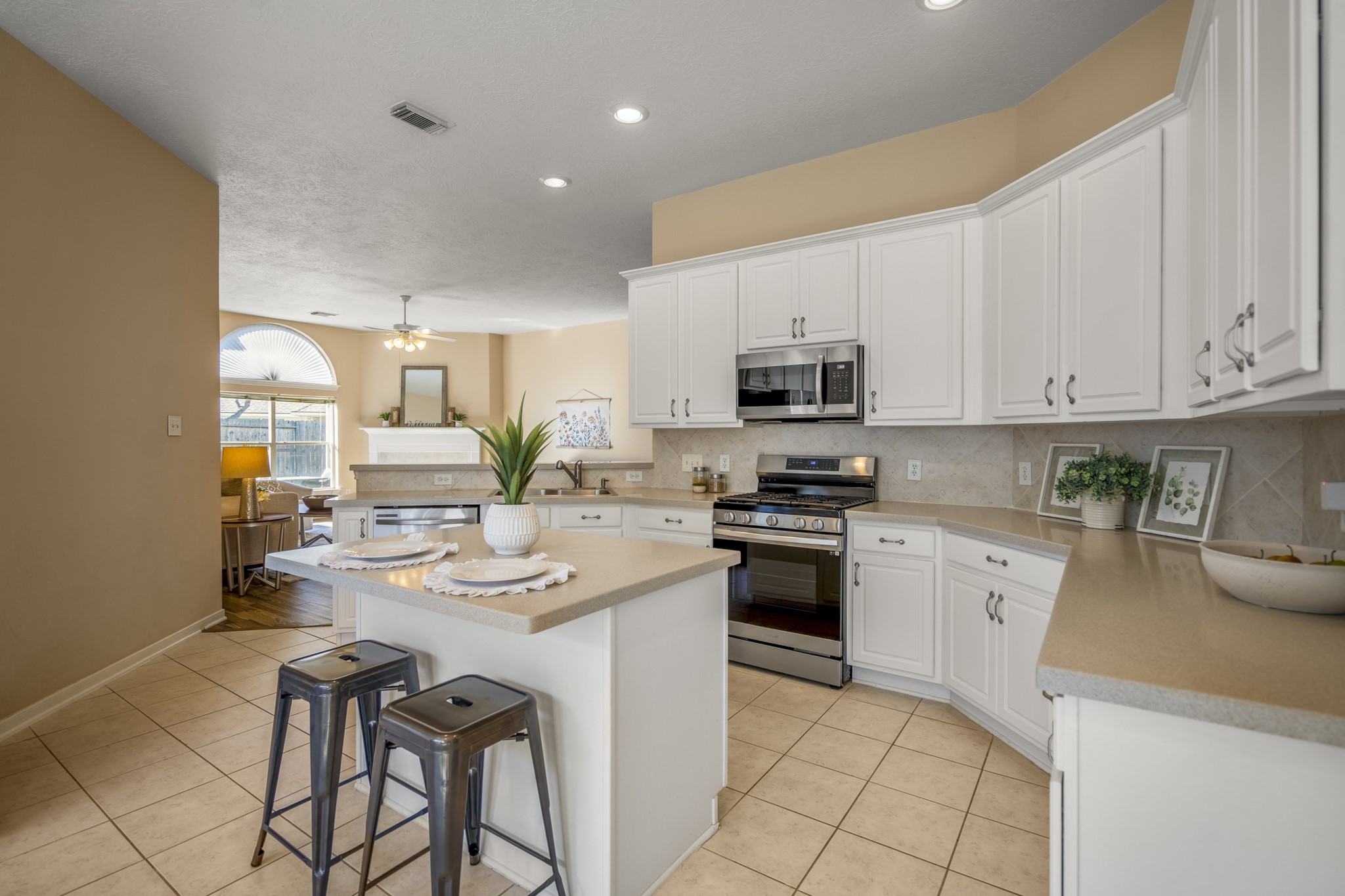 21107 Coldde Meadow Lane Spring, TX 77379 - Photo 13 of 50 Moving around the island, this view opens back toward the living room, showing how the kitchen stays connected to the main gathering space. The raised bar along the counter creates a natural place for casual seating while keeping the cook part of the conversation happening just beyond.
