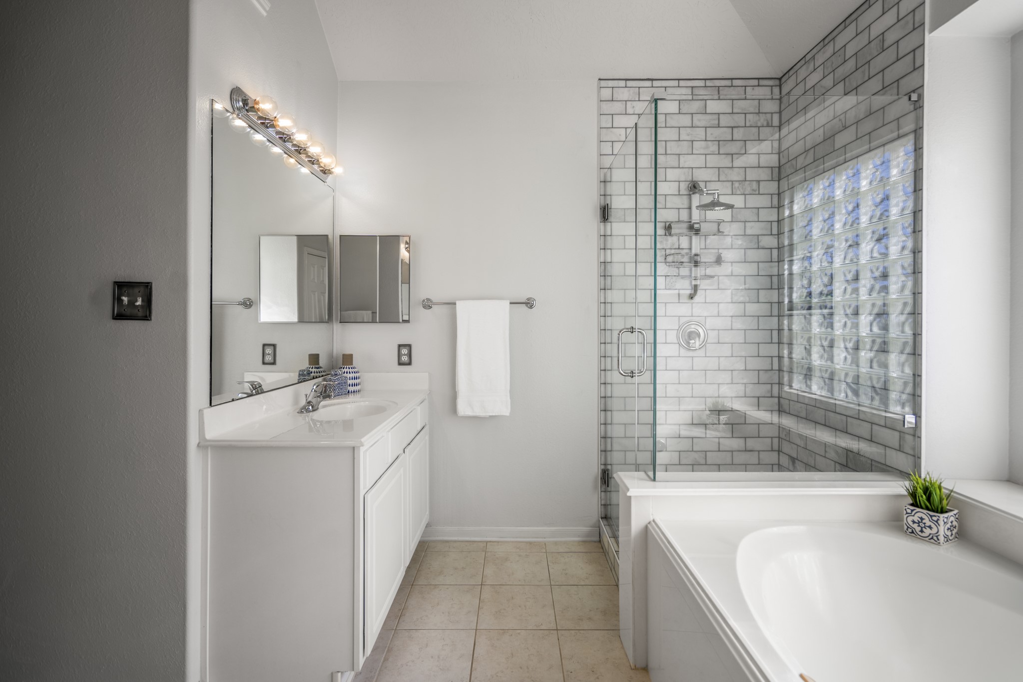 21107 Coldde Meadow Lane Spring, TX 77379 - Photo 25 of 50 This view highlights one of the two separate vanity areas in the primary bathroom, offering its own sink, counter space, and storage. Just beyond, the walk-in shower features updated tile and a frameless glass enclosure, adding a refreshed look to the space while the soaking tub sits nearby.