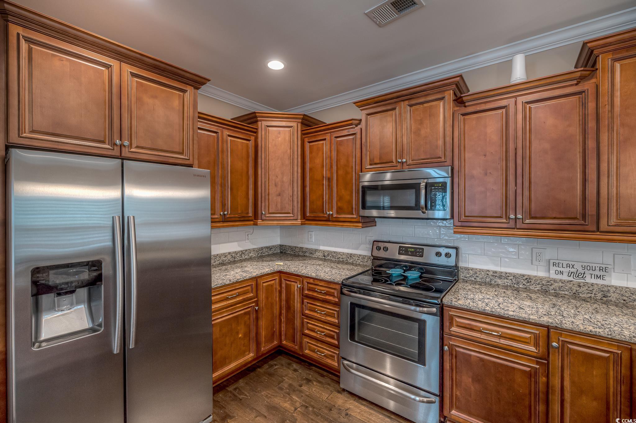 103 Charles Towne Lane Murrells Inlet, SC 29576 - Photo 12 of 23 Kitchen featuring appliances with stainless steel finishes, crown molding, dark wood-style flooring, tasteful backsplash, and light stone countertops