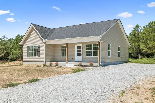 a front view of a house with a dirt road and trees