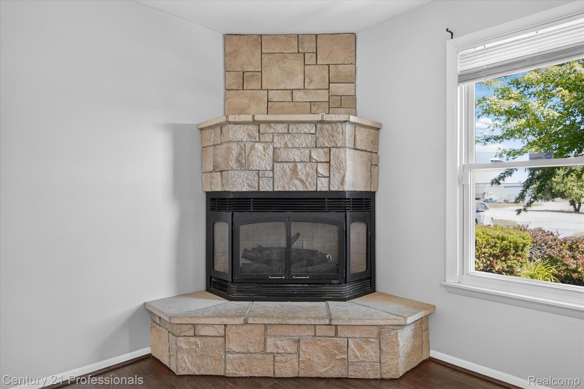648 Newport Road Carleton, MI 48117 - Photo 10 of 37 Corner fireplace with stone surround and hearth, featuring a black firebox and integrated screen