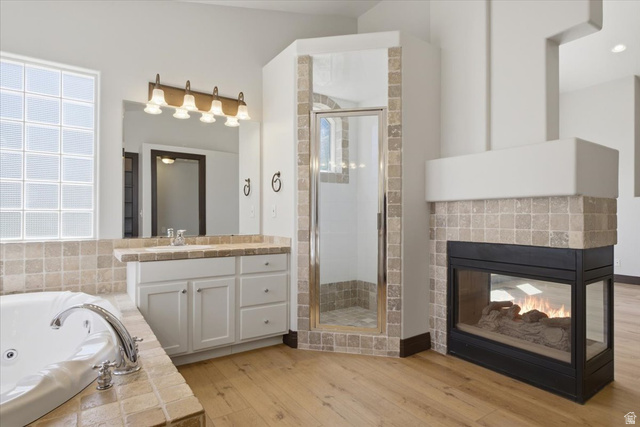 12317 Cypress Point Way Draper, UT 84020 - Photo 18 of 41 Bathroom featuring a corner shower with glass enclosure, a built-in jetted tub with tiled surround, a vanity with under-sink cabinetry and a light-toned countertop, a glass block window, and a built-in fireplace with a tiled hearth and mantel