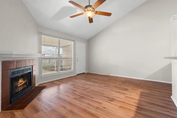 a view of an empty room with wooden floor fireplace and a window