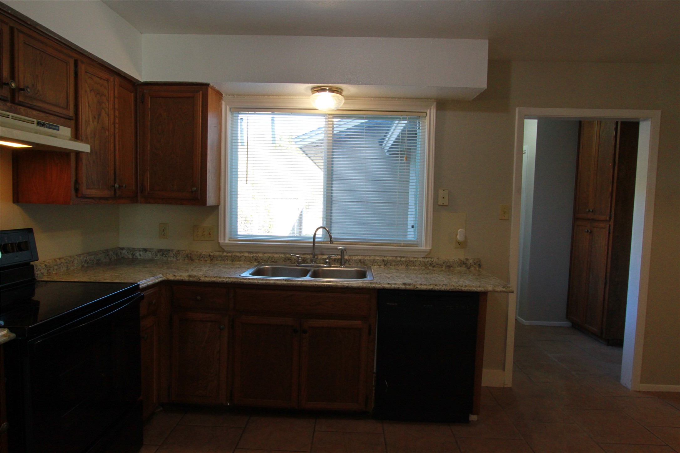 3904 Hudson Bend Road, Unit D Austin, TX 78734 - Photo 10 of 25 Kitchen featuring black appliances, under cabinet range hood, dark tile patterned floors, and brown cabinetry