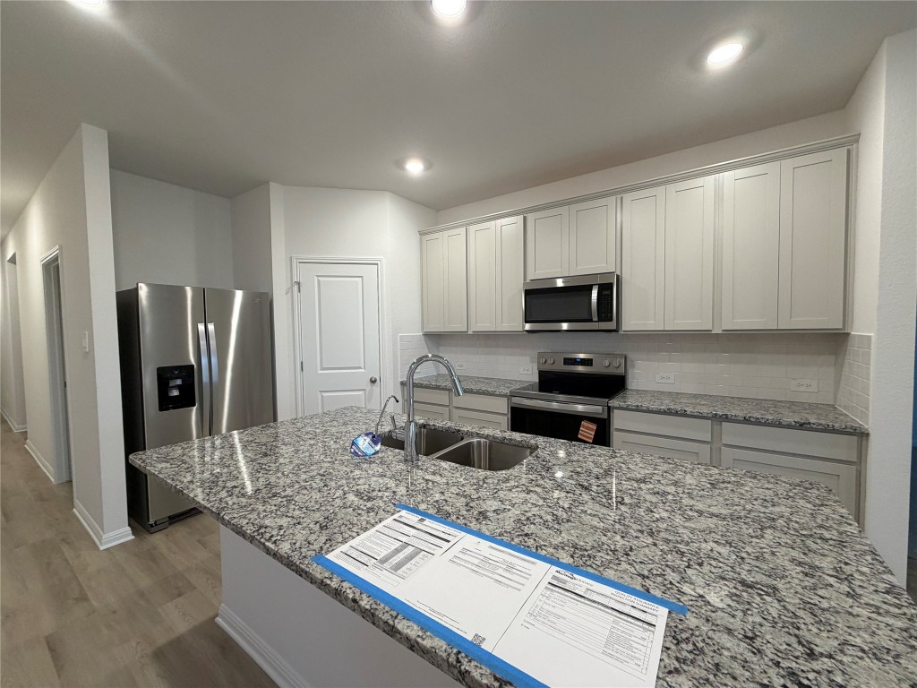 100 Honey Bee Road Jarrell, TX 76537 - Photo 6 of 17 Kitchen with light stone countertops, appliances with stainless steel finishes, tasteful backsplash, a center island with sink, and light wood-style flooring