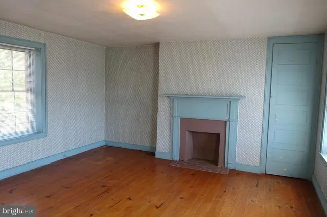 an empty room with wooden floor fireplace and windows