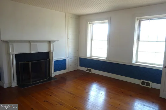 an empty room with wooden floor fireplace and windows