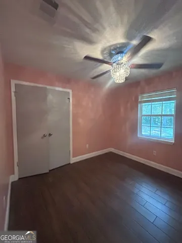 an empty room with wooden floor chandelier fan and windows