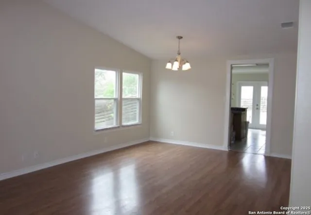 an empty room with wooden floor chandelier and windows