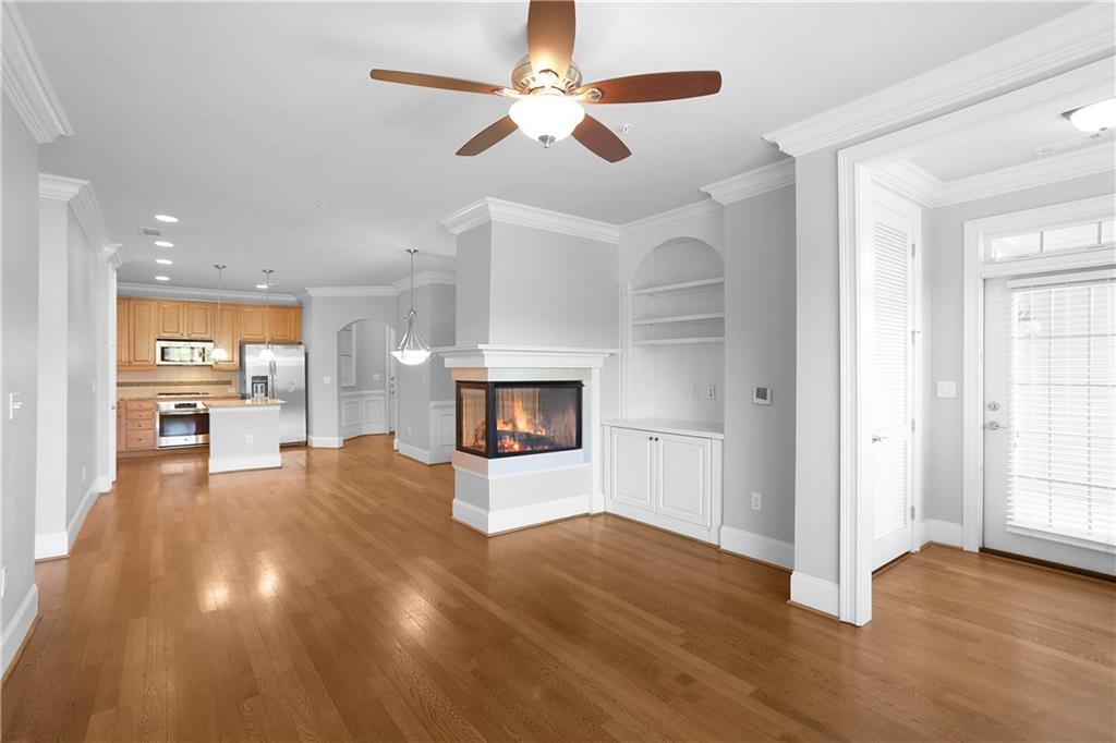 an empty room with wooden floor a ceiling fan and kitchen view