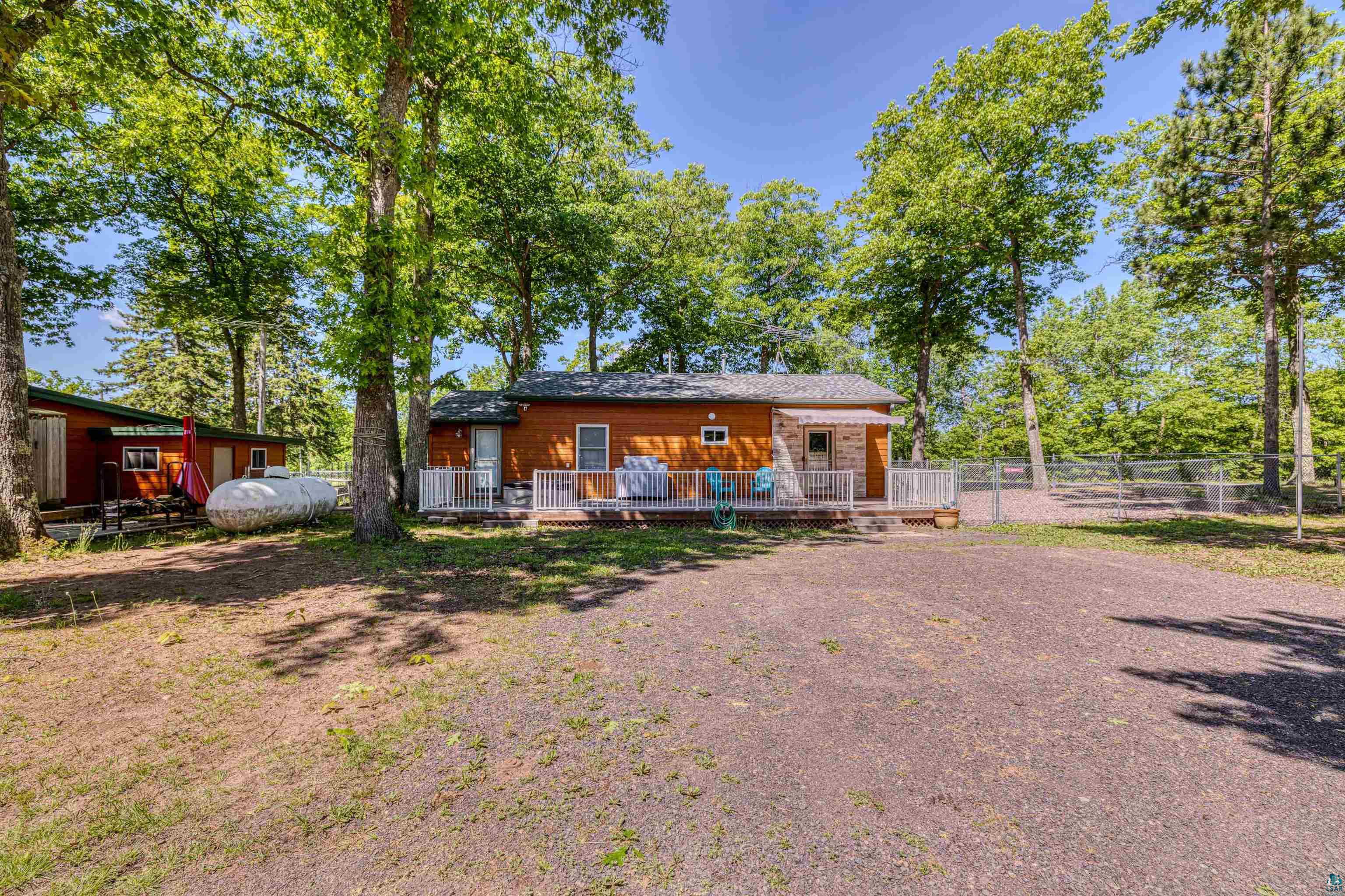 66075 Rooster Road Iron River, WI 54847 - Photo 38 of 52 Cedar-sided residence featuring a front deck with white railings, a gravel driveway, and mature trees