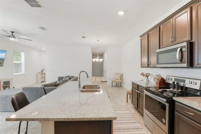 a kitchen with stainless steel appliances granite countertop a sink a stove top oven a dining table and chairs with wooden floor