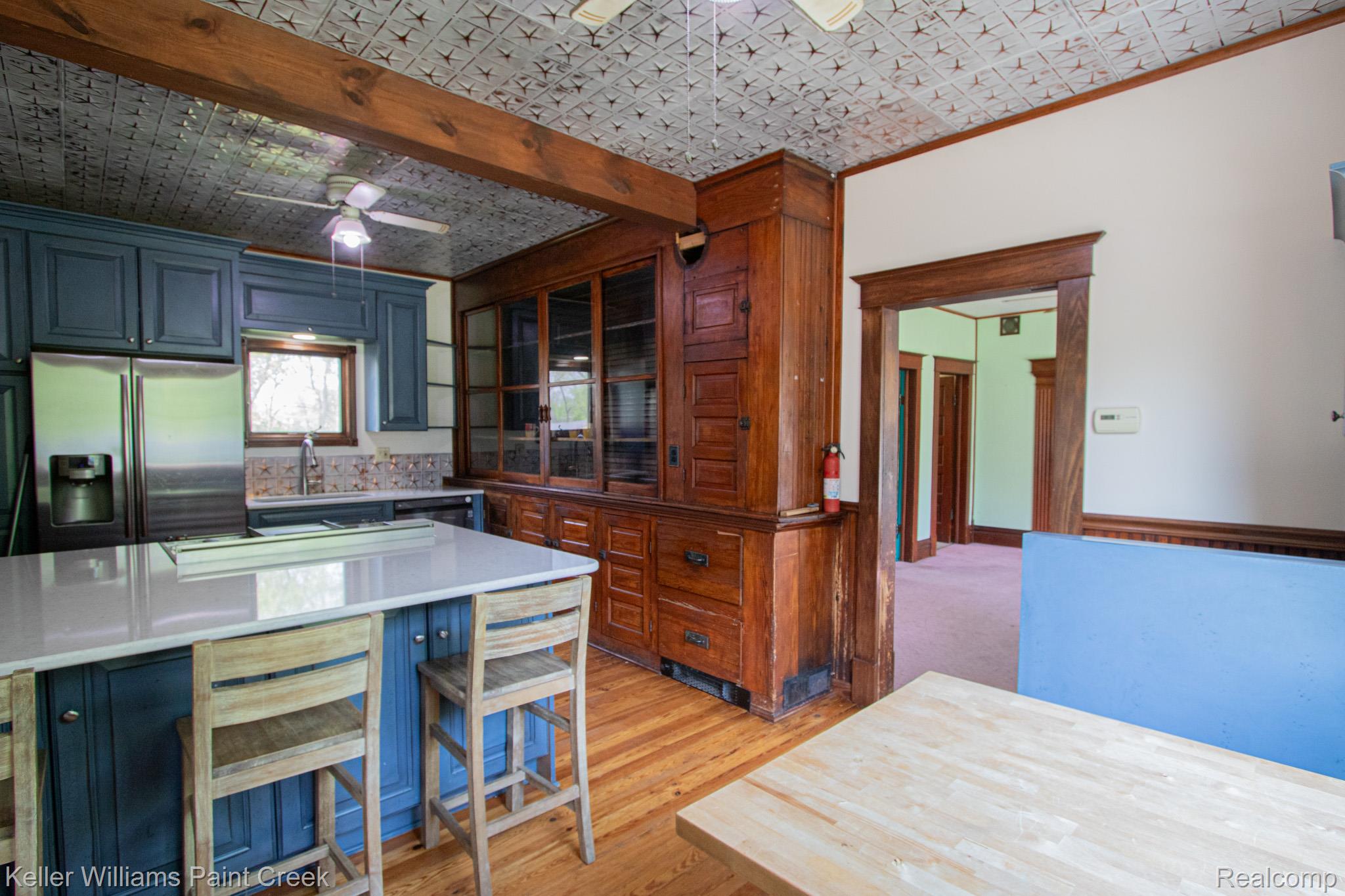 Kitchen featuring ceiling fan, stainless steel fridge with ice dispenser, light wood-style floors, a breakfast bar area, and an ornate ceiling