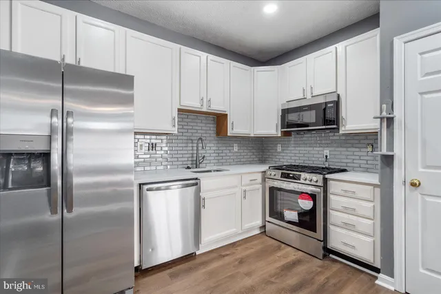 a kitchen with stainless steel appliances granite countertop a refrigerator a stove a sink and white cabinets