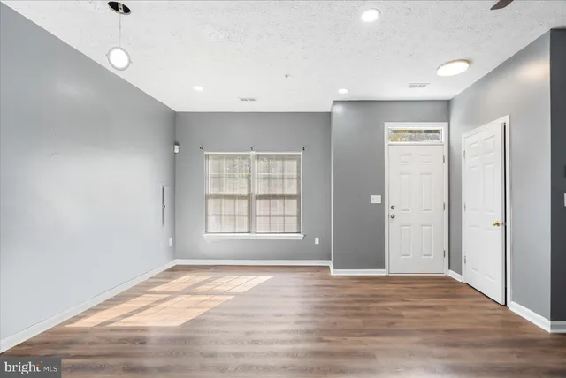 a view of an empty room with wooden floor and a window