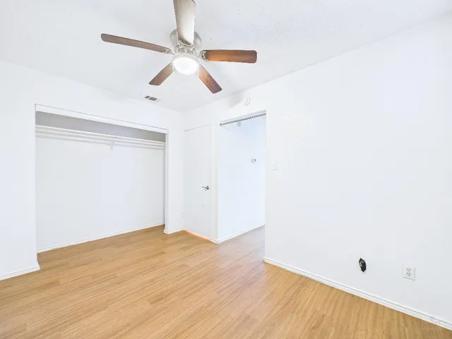 an empty room with wooden floor fan and windows