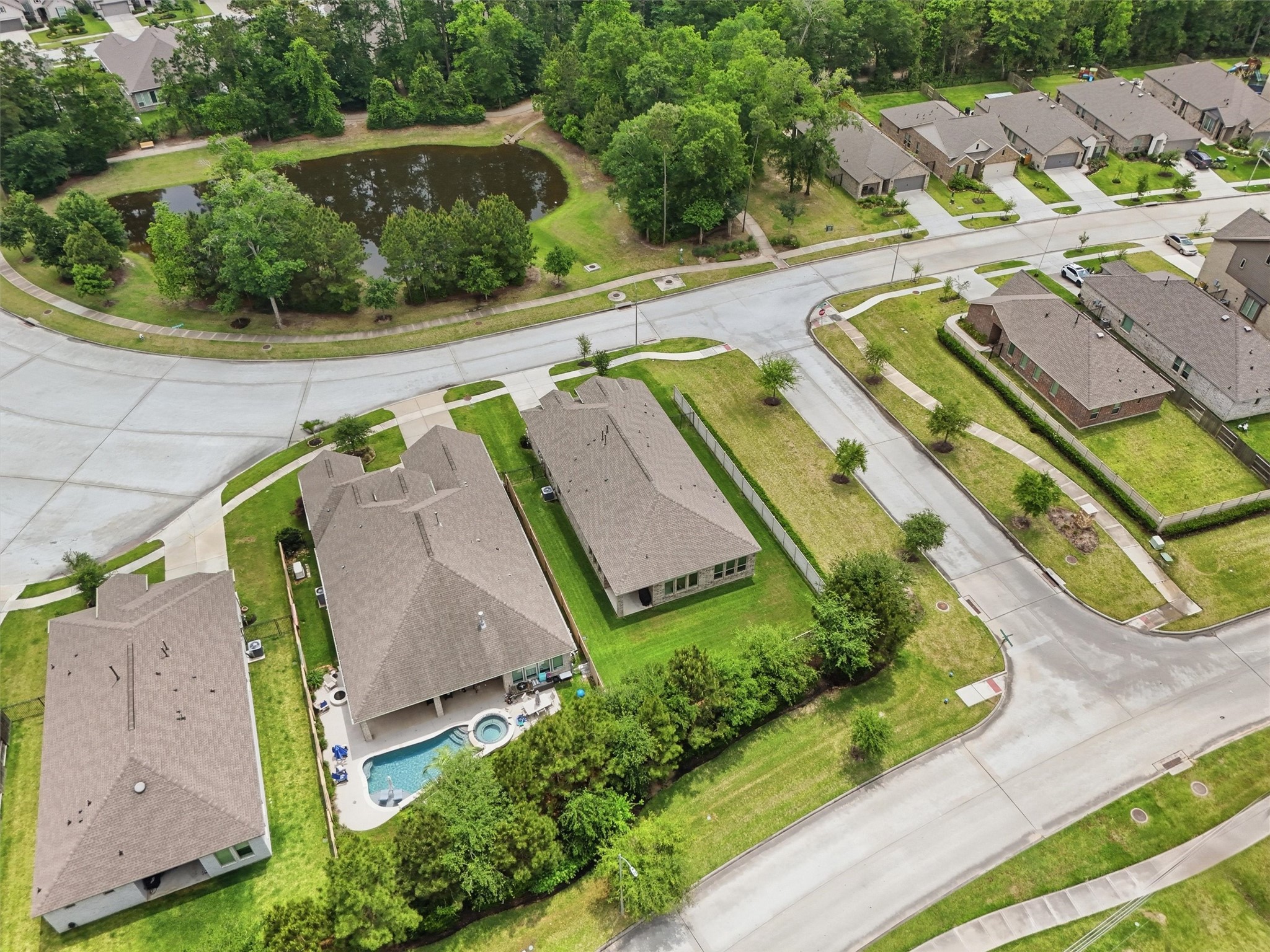 6071 Windward Falls Way Porter, TX 77365 - Photo 30 of 33 This aerial view showcases a serene neighborhood with spacious single-story homes, well-maintained lawns. The area is lush with greenery and features a nearby pond, offering a tranquil setting ideal for families.