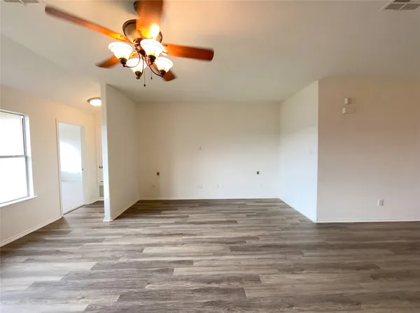 a view of an empty room with wooden floor and a chandelier fan