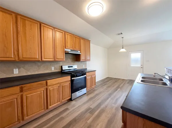 a kitchen with stainless steel appliances granite countertop wooden cabinets a stove a sink and dishwasher with wooden floor