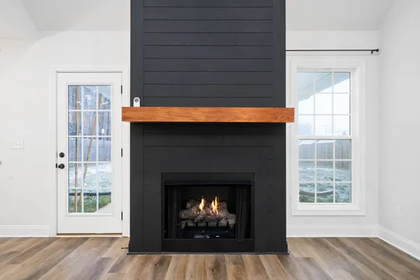 a view of an empty room with wooden floor fireplace and a window