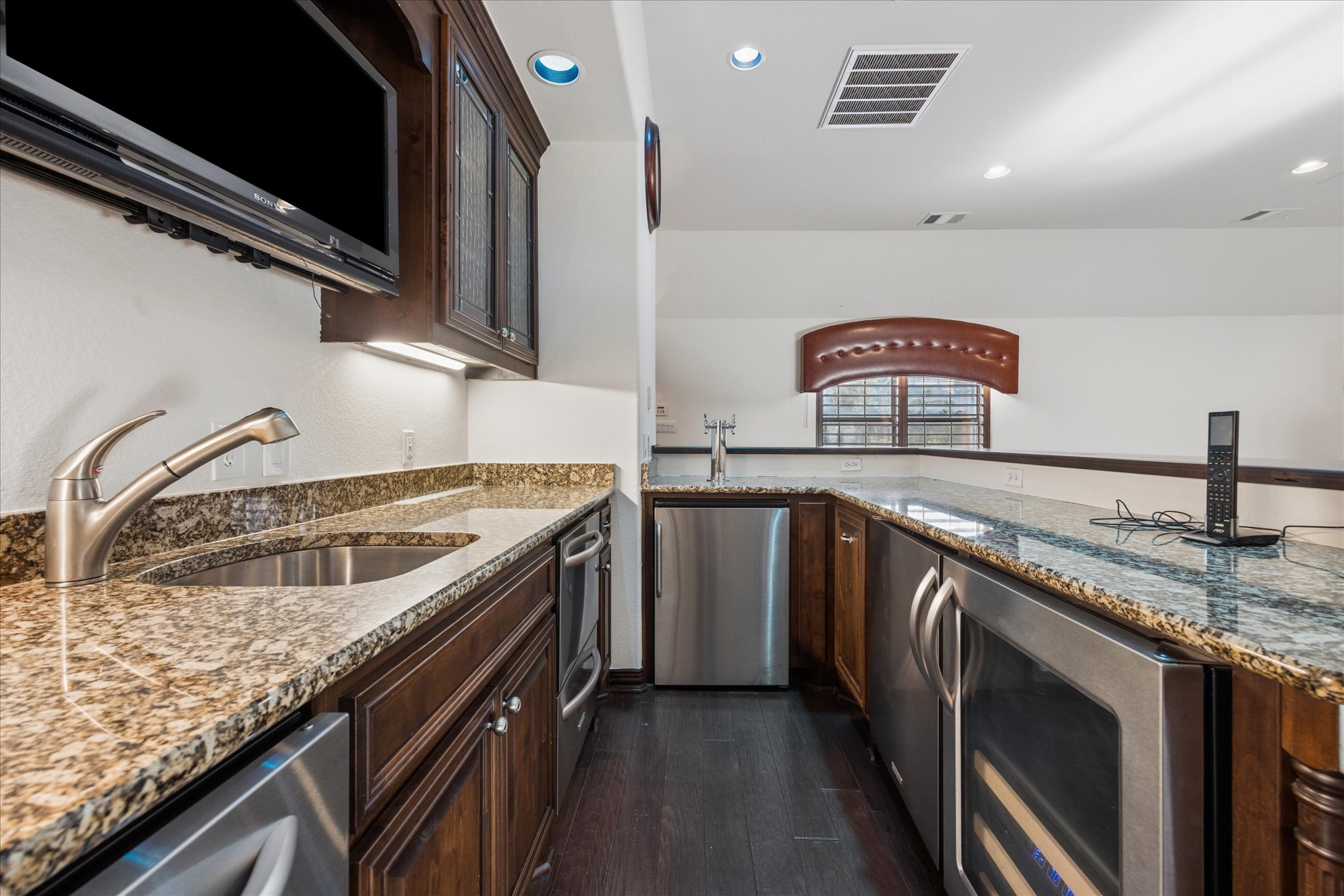 11805 Ranchview Court Austin, TX 78732 - Photo 22 of 36 Wet bar featuring granite countertops, a stainless steel sink with pull-down faucet, rich wood cabinetry, and integrated stainless steel appliances