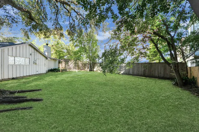 a view of a backyard with large trees and wooden fence