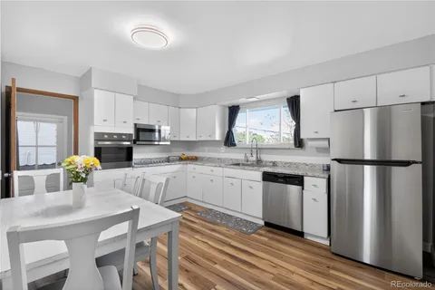 a kitchen with refrigerator a stove a sink and white cabinets with wooden floor