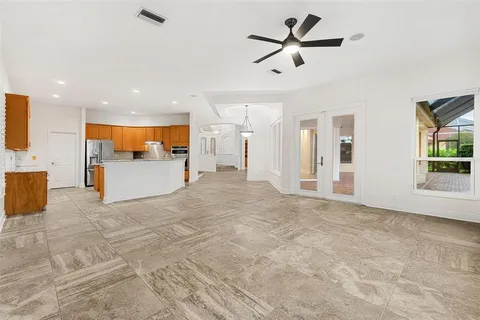 a view of an empty room with a chandelier fan and kitchen view