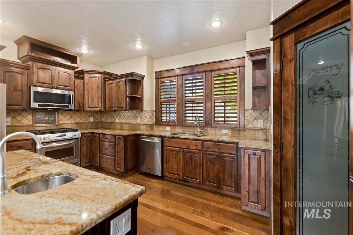 2543 West Divide Creek Street Meridian, ID 83646 - Photo 12 of 49 Kitchen with open shelves, light stone counters, backsplash, stainless steel appliances, and dark wood finished floors