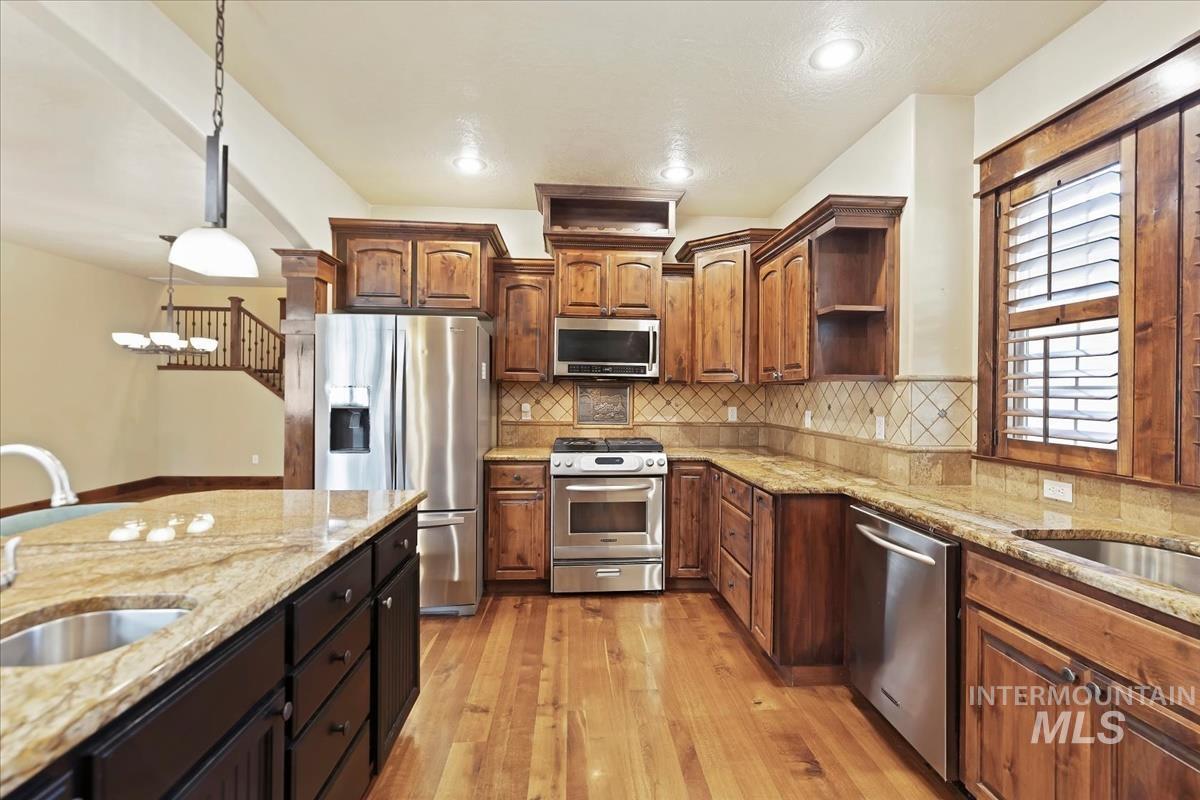 2543 West Divide Creek Street Meridian, ID 83646 - Photo 13 of 49 Kitchen with light stone counters, appliances with stainless steel finishes, decorative light fixtures, light wood finished floors, and tasteful backsplash