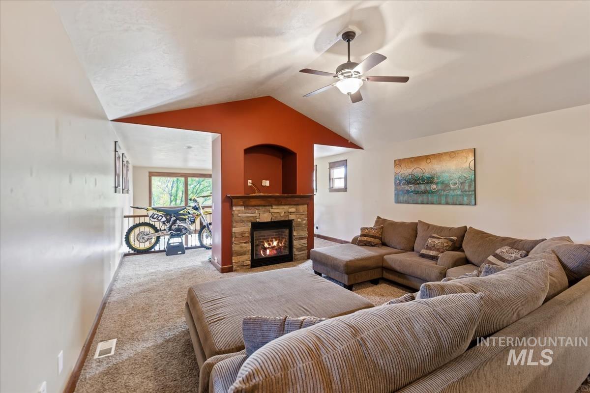 2543 West Divide Creek Street Meridian, ID 83646 - Photo 30 of 49 Living area with carpet flooring, healthy amount of natural light, vaulted ceiling, a stone fireplace, and a ceiling fan