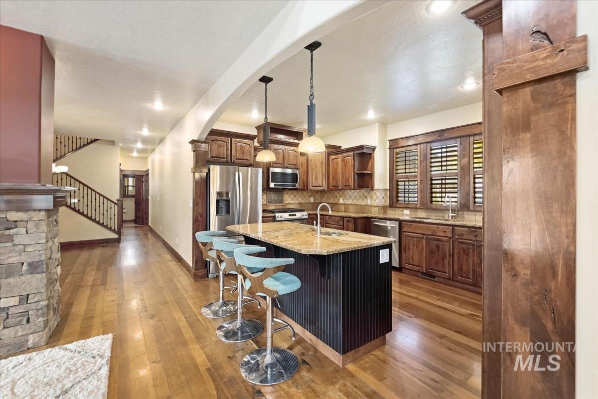2543 West Divide Creek Street Meridian, ID 83646 - Photo 10 of 49 Kitchen with a center island with sink, a breakfast bar area, open shelves, light stone counters, and hanging light fixtures